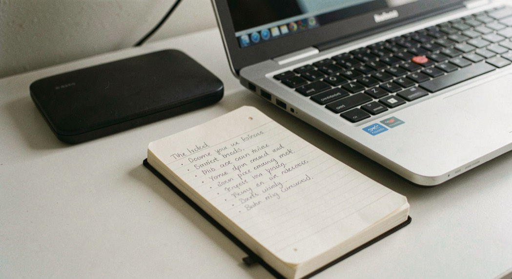 Bloc-notes ouvert avec une liste manuscrite à côté d’un ordinateur portable fermé sur un plan de travail clair